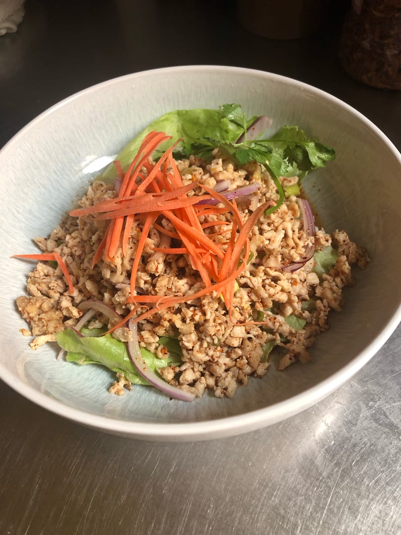 A bowl of Thai larb gai with minced chicken, red onion, cilantro, carrots, and lettuce.