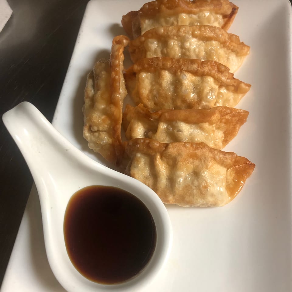 Crispy fried dumplings arranged on a white plate with a small bowl of dark dipping sauce.