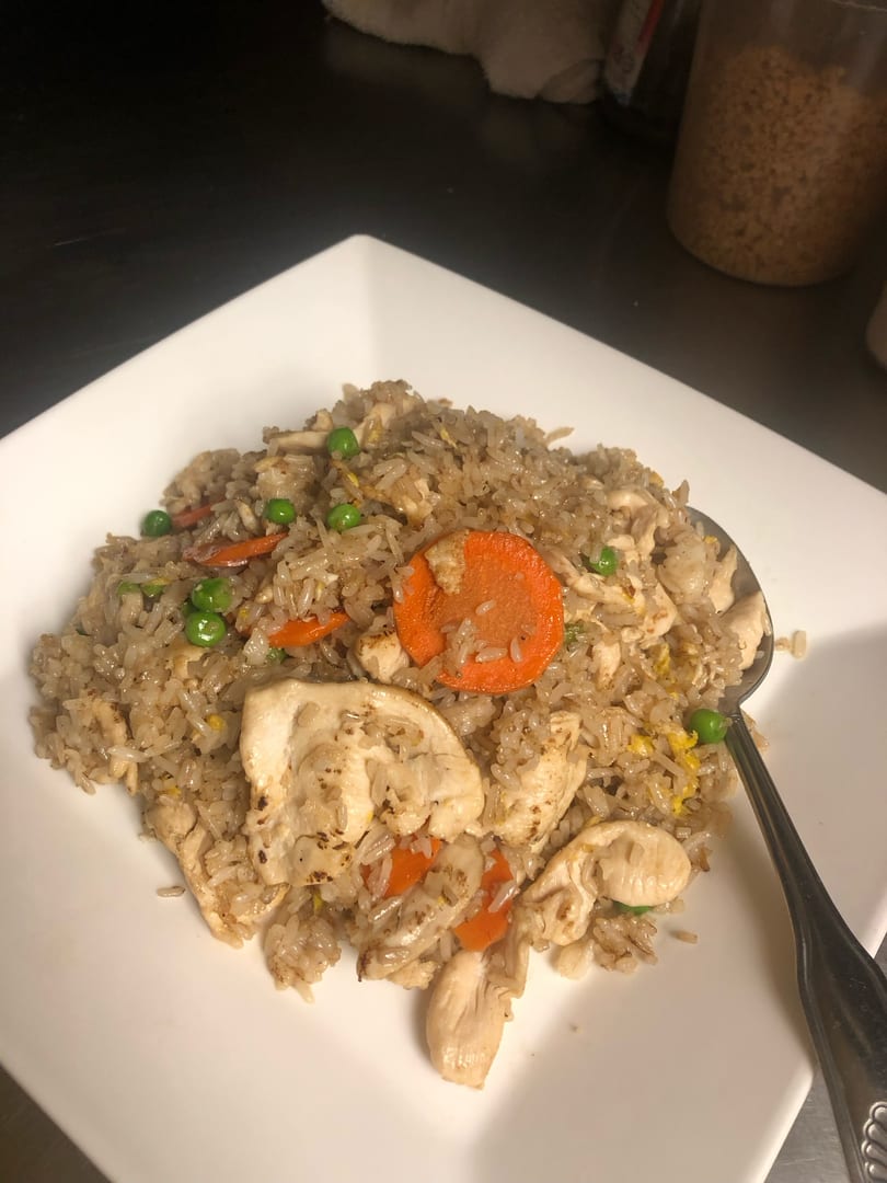 Chicken fried rice with peas and carrots on a white square plate with a spoon.