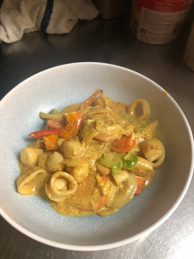 A bowl of seafood curry with scallops, shrimp, calamari, and bell peppers in a rich yellow sauce.