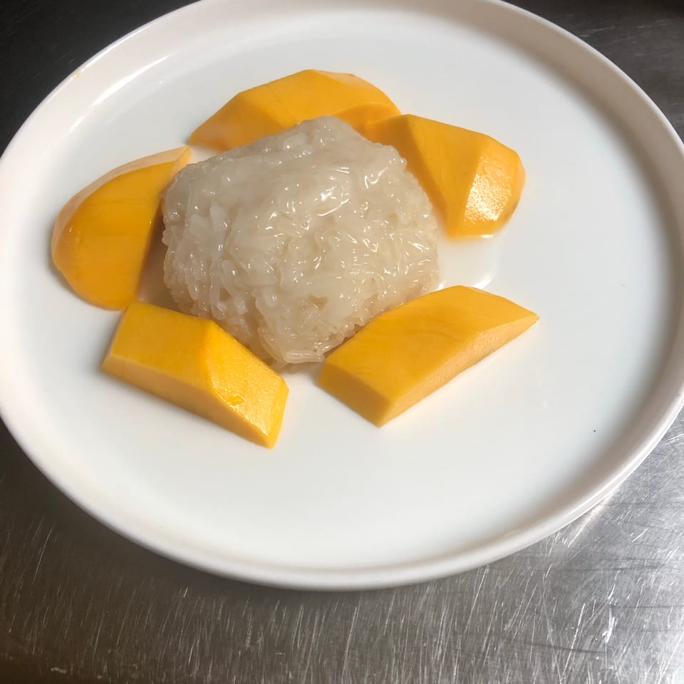 Sticky rice topped with mango slices on a white plate.
