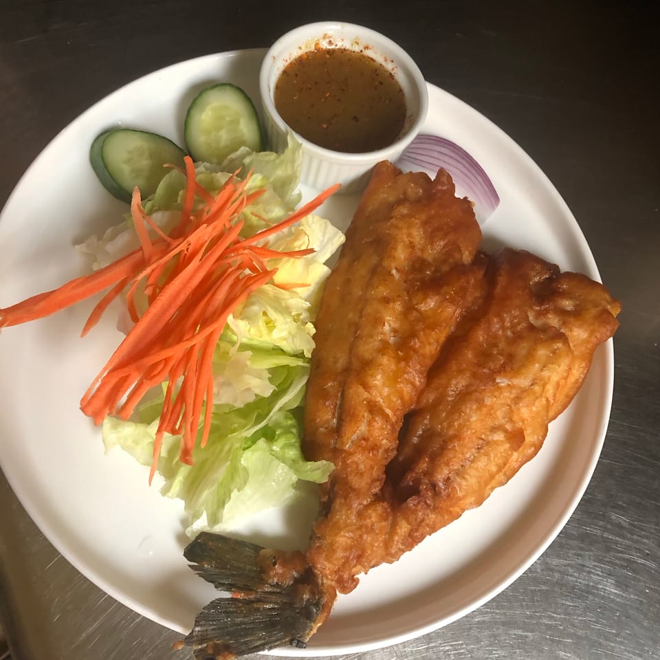Crispy fried fish served with lettuce, shredded carrots, cucumber, red onion, and a small bowl of dipping sauce.