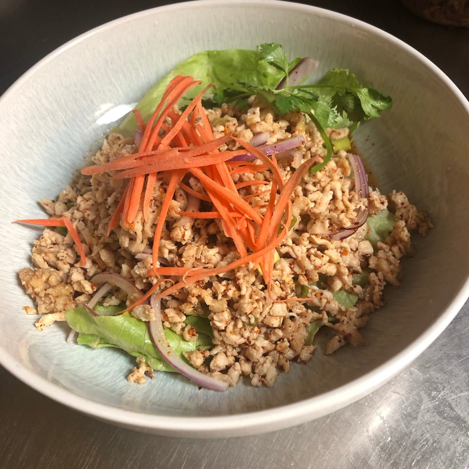 Bowl of seasoned minced meat salad with lettuce, shredded carrots, red onion, cucumber, and fresh cilantro.