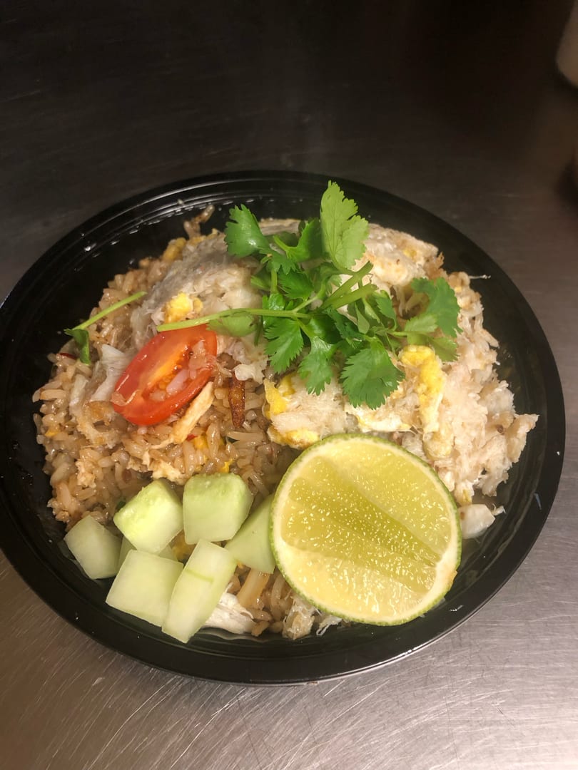 Crab fried rice with cilantro, tomato, cucumber, and lime in a black bowl.