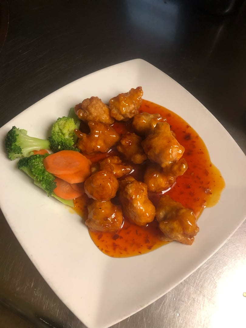 Sweet and sour chicken with broccoli and carrots on a white square plate.