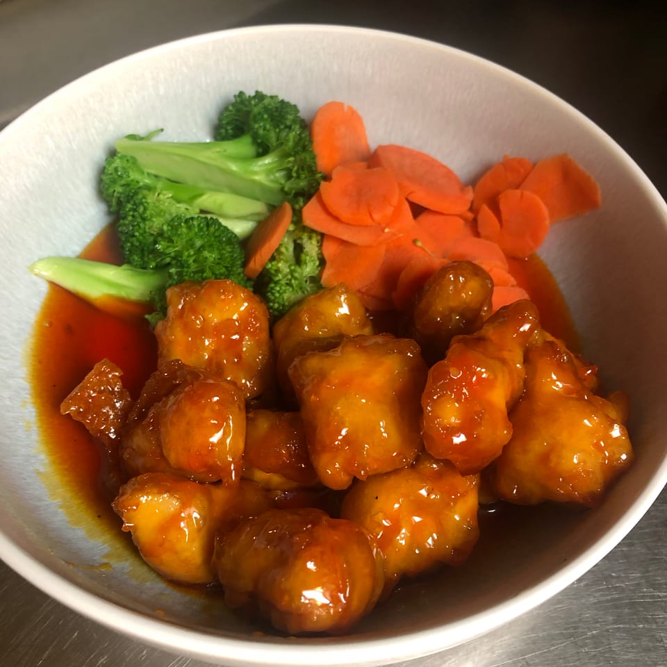 Bowl of glossy orange-glazed chicken pieces served with broccoli and sliced carrots.