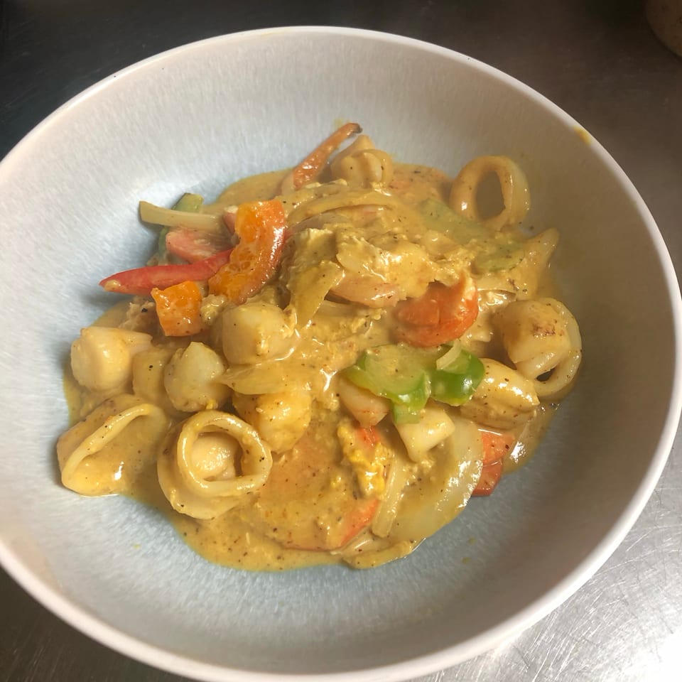 Creamy seafood pasta with shrimp, calamari, chicken, potatoes, and colorful peppers served in a white bowl.