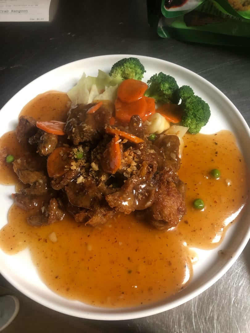 A white plate holds fried meat in orange sauce with broccoli, carrots, and cabbage.
