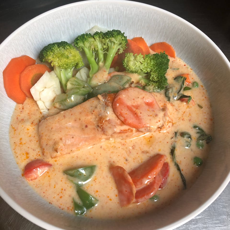 Creamy sauce coats salmon and mixed vegetables, including broccoli, carrots, cauliflower, tomatoes, and green peppers in a bowl.