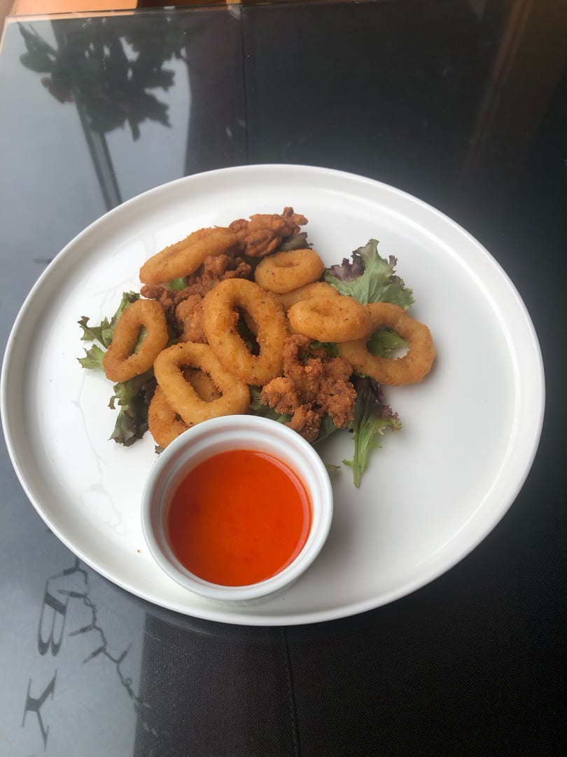 Crispy fried calamari rings and pieces on a bed of lettuce with a side of red dipping sauce.
