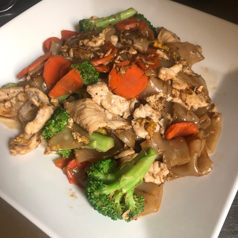 Stir-fried chicken with broccoli, carrots, onions, and peppers served on a white plate.